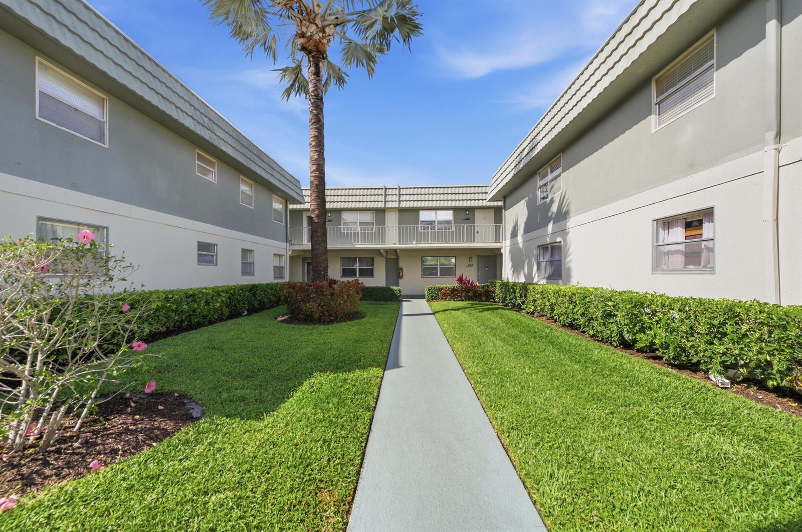 A palm tree stands in a grassy courtyard between two multi-story apartment buildings — 284 Flanders F, Delray Beach FL 33484, DELRAY BEACH, FL
