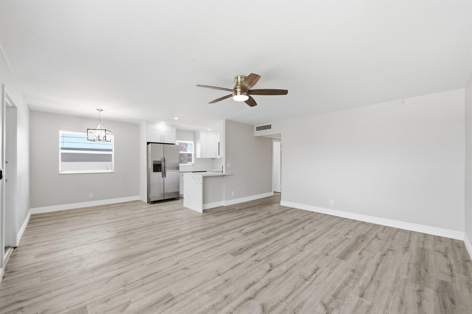 An open-concept living and dining area features light wood-look flooring, white walls, and a kitchen — 284 Flanders F, Delray Beach FL 33484, DELRAY BEACH, FL