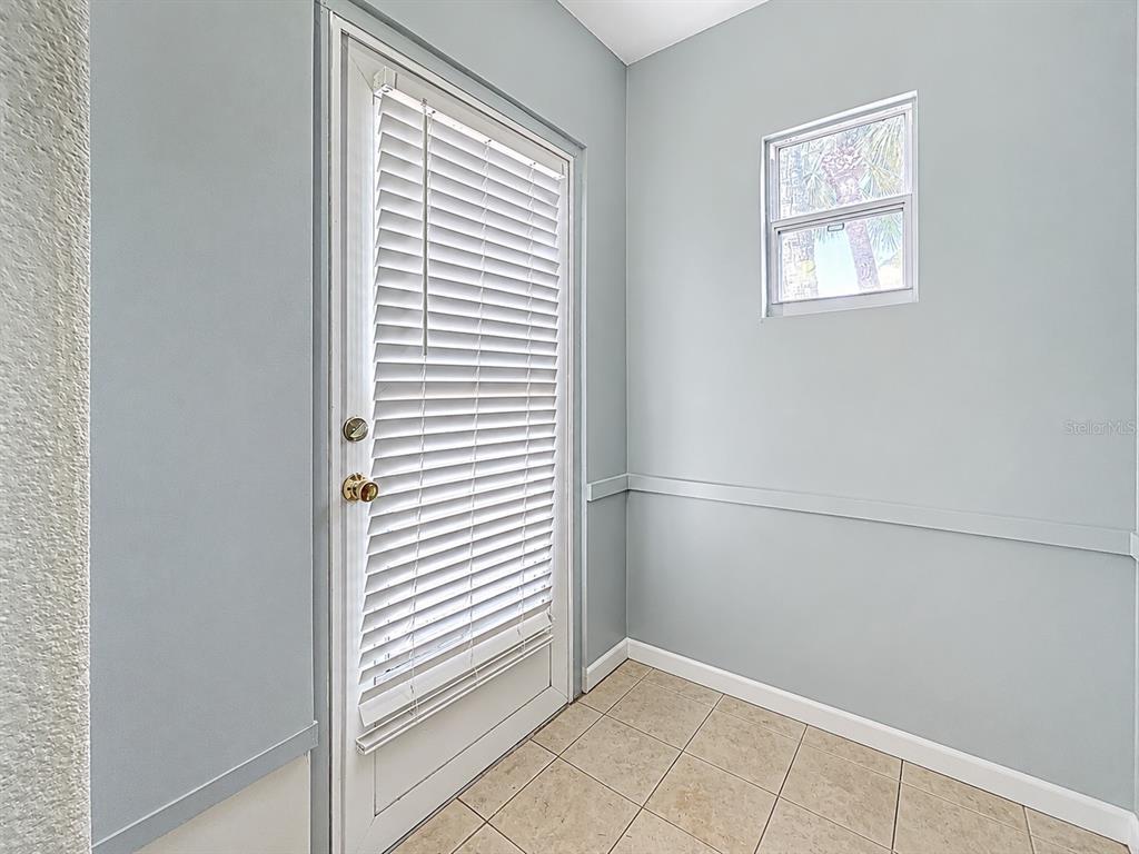 A small room with light blue walls, tile flooring, a window, and a white door — 250 ROSERY ROAD NW UNIT 228, LARGO, FL