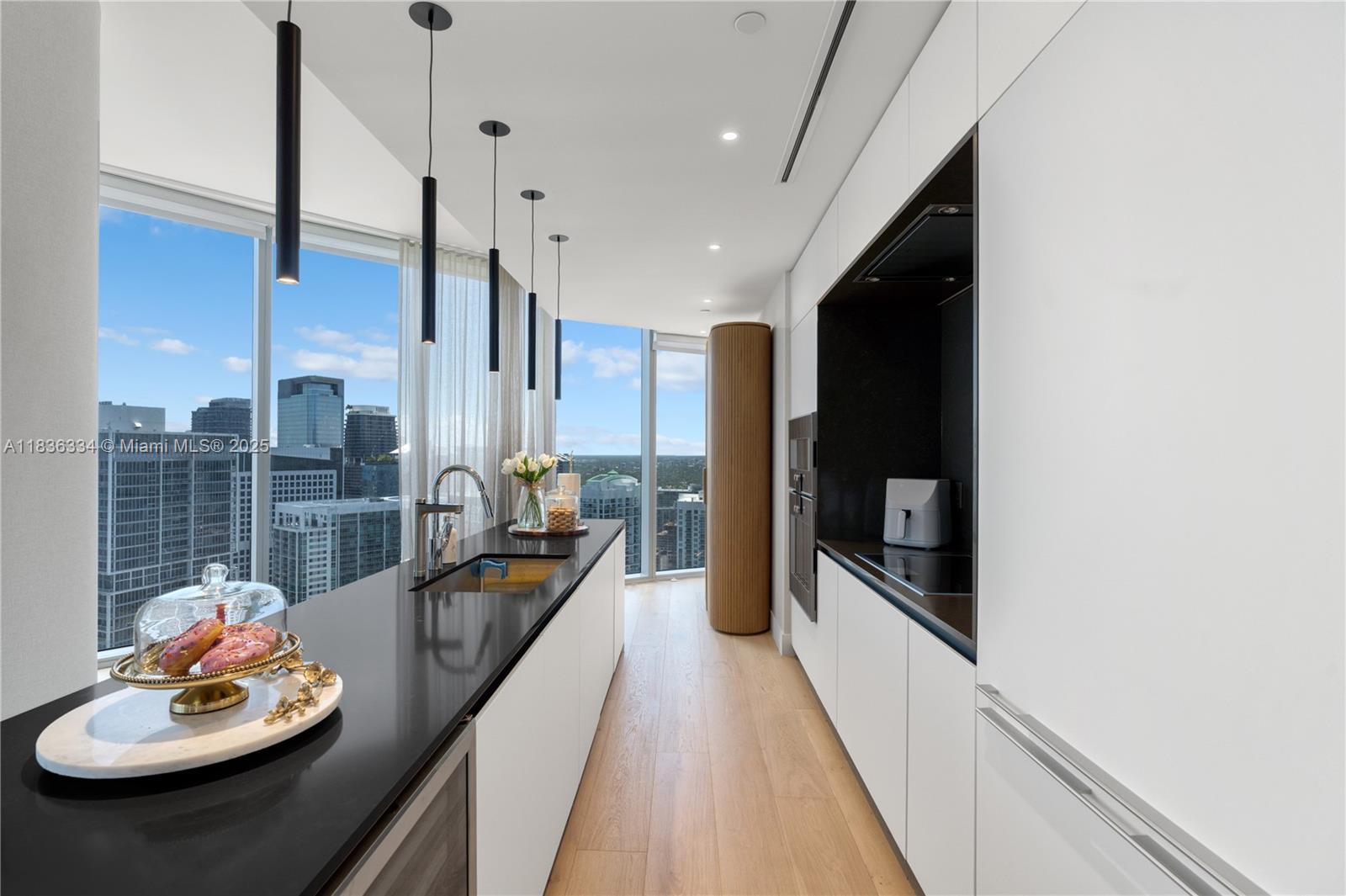 A modern kitchen features white cabinetry, a black countertop, and floor-to-ceiling windows with city views — 300 Biscayne Blvd way # 4707, Miami FL 33131, MIAMI, FL