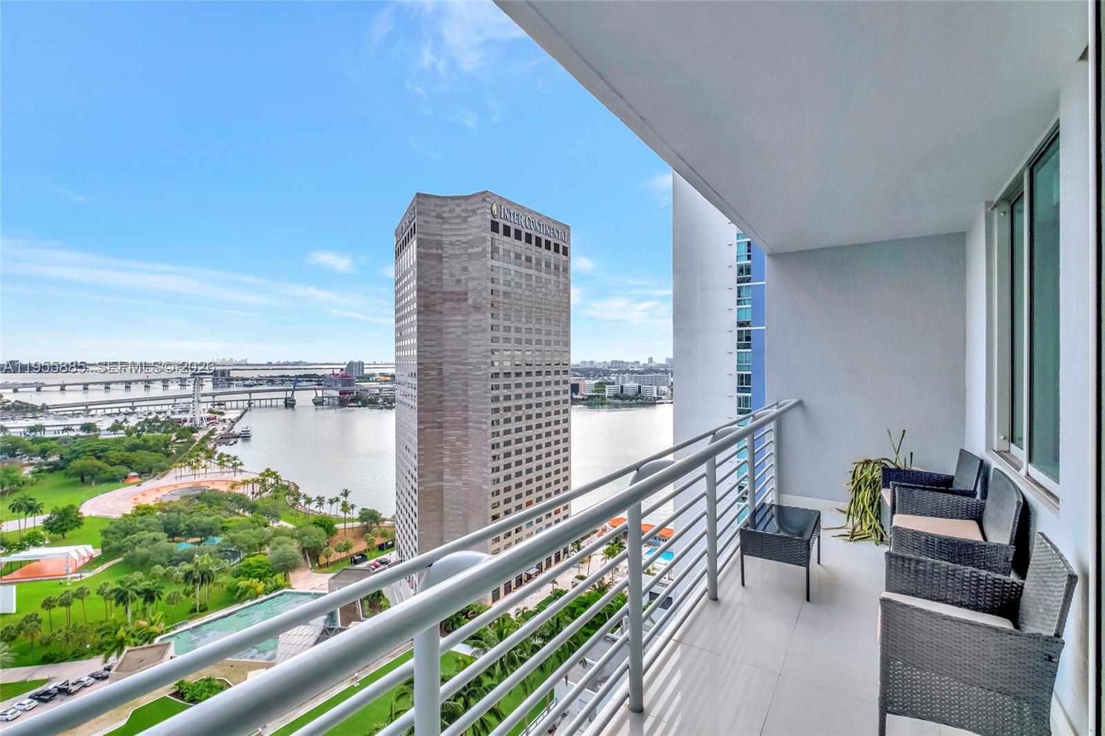 A balcony with outdoor furniture overlooks a large hotel building, a park, and a bay — 325 S Biscayne Blvd # 2616, Miami FL 33131, MIAMI, FL