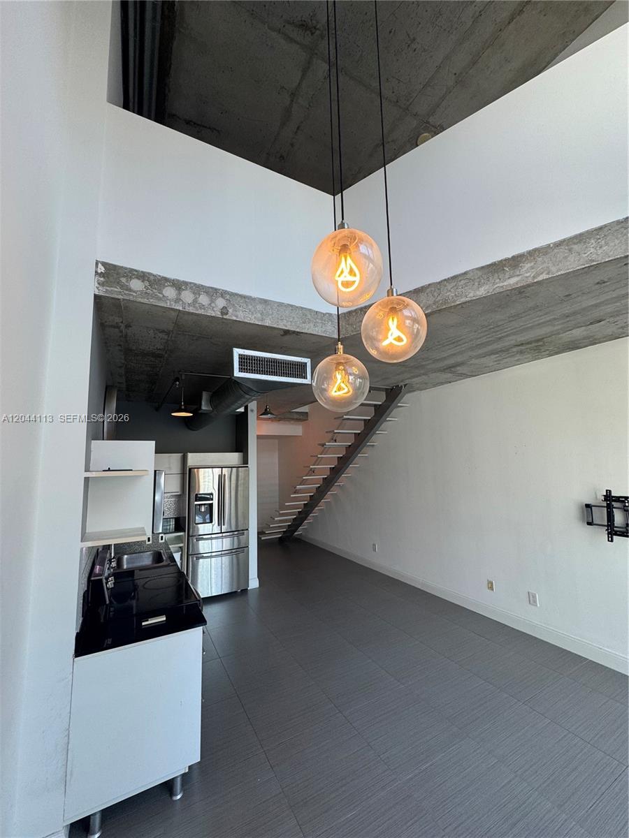 A modern kitchen and living area feature high ceilings, exposed concrete, and a floating staircase — 690 SW 1st Ct # 1516, Miami FL 33130, MIAMI, FL