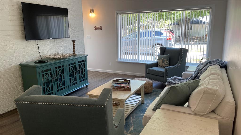 A living room features a white brick wall, a teal media console, and neutral furniture — 2504 S MILMAR DRIVE, SARASOTA, FL