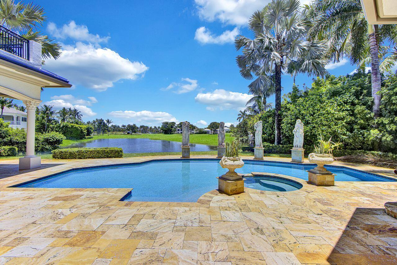 A swimming pool with stone decking and statues overlooks a lake on a sunny day — 17730 Scarsdale Way, Boca Raton FL 33496, BOCA RATON, FL