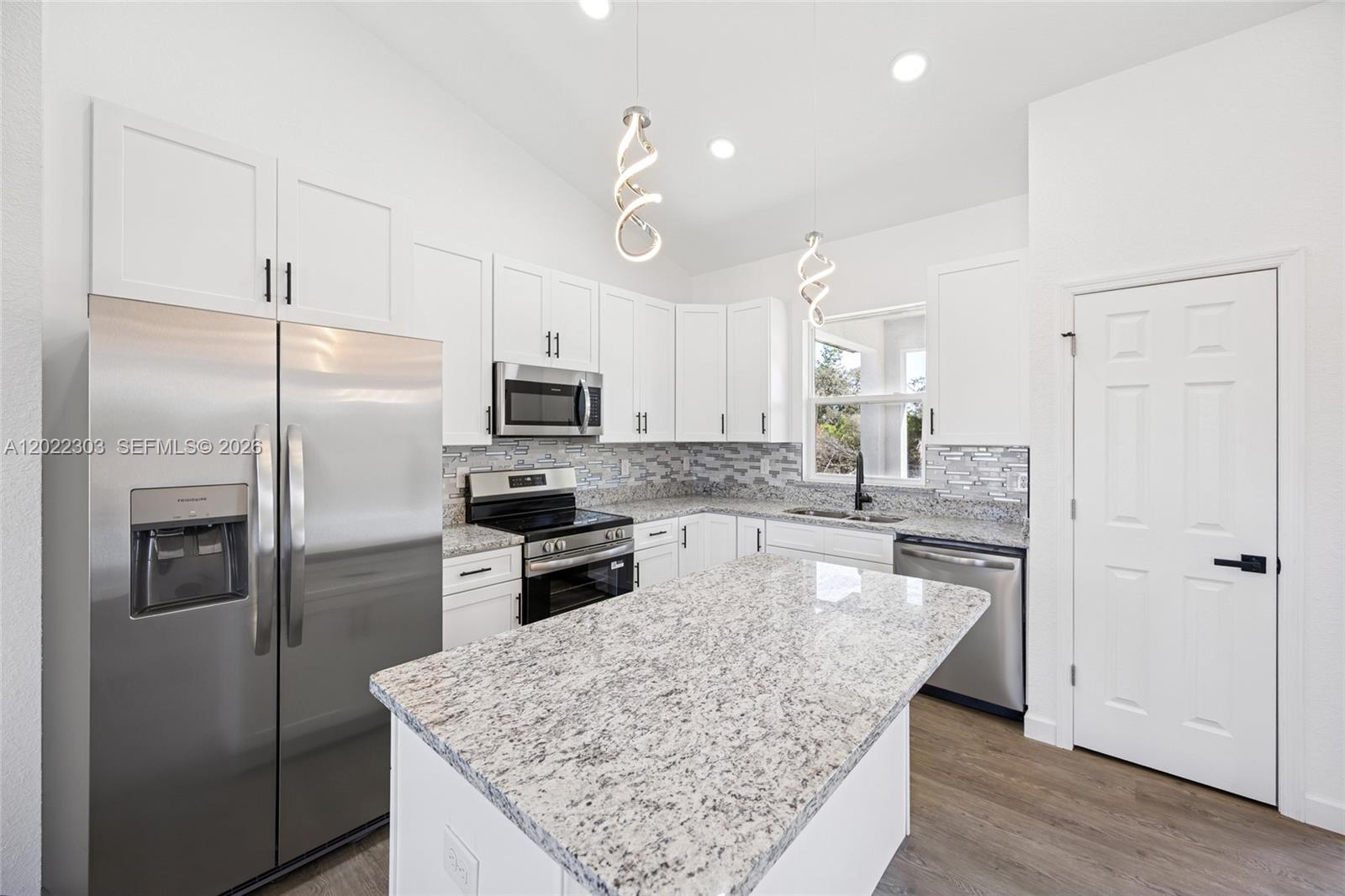 A modern kitchen features white cabinets, granite countertops, stainless steel appliances, and a central island — 7433 DOMENICO ST, Sebring FL 3872, SEBRING, FL