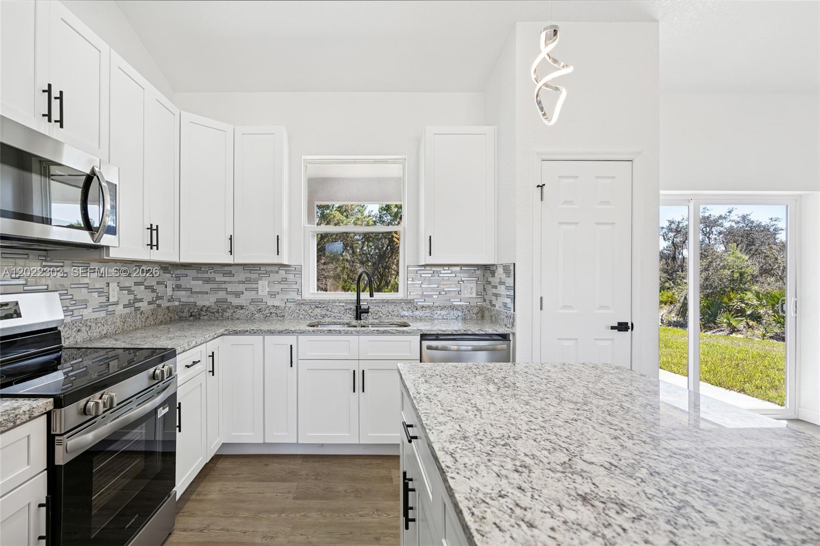 A kitchen features white cabinets, granite countertops, a tiled backsplash, and stainless steel appliances — 7433 DOMENICO ST, Sebring FL 3872, SEBRING, FL
