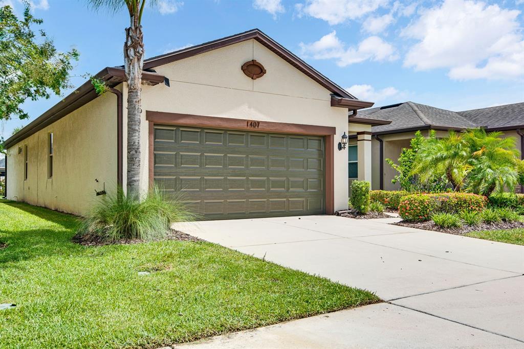 A single-story house with a beige stucco exterior, a brown garage door, and a driveway — 1407 CUSTER BAYOU STREET, RUSKIN, FL
