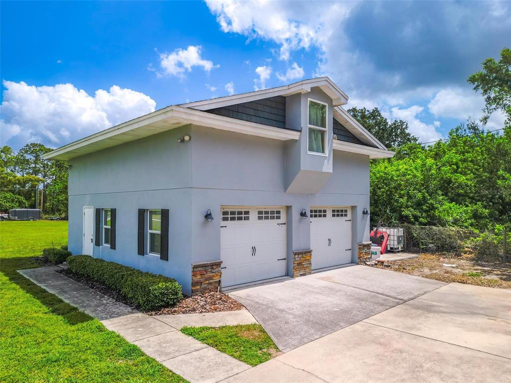 A two-story detached garage with a light gray exterior, stone accents, and two white doors — 250 BRIGHAM ROAD NW, WINTER HAVEN, FL