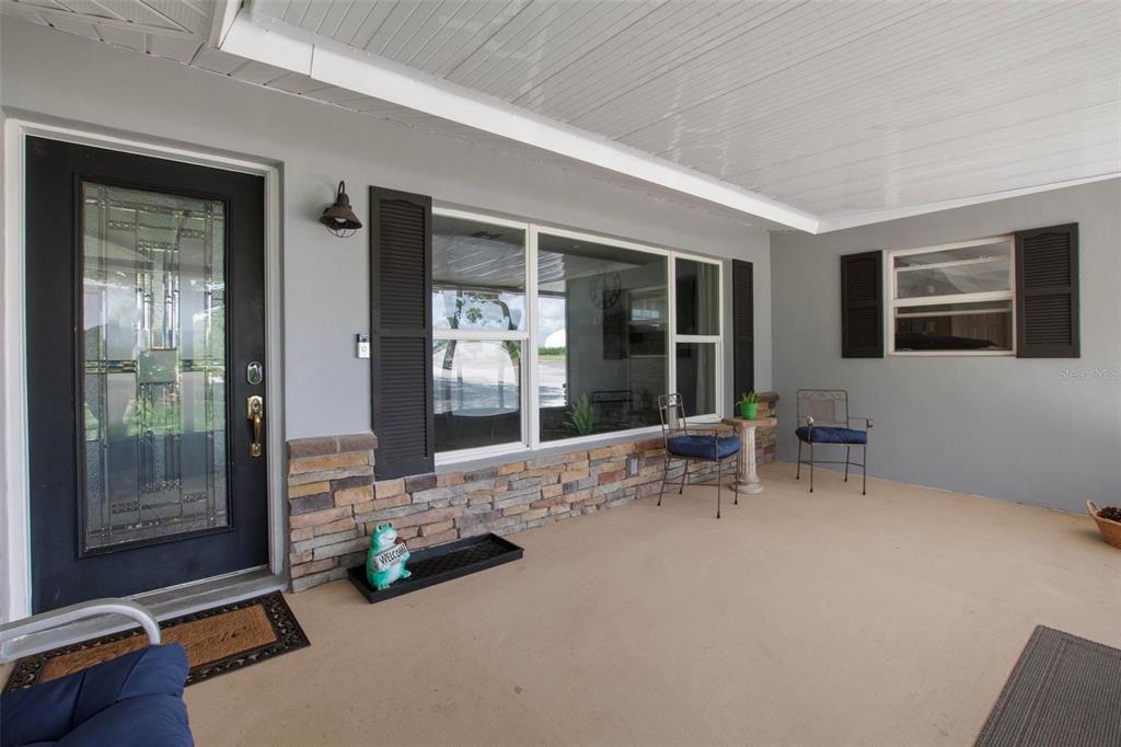A covered front porch features a black front door, stone siding, and two metal chairs — 250 BRIGHAM ROAD NW, WINTER HAVEN, FL