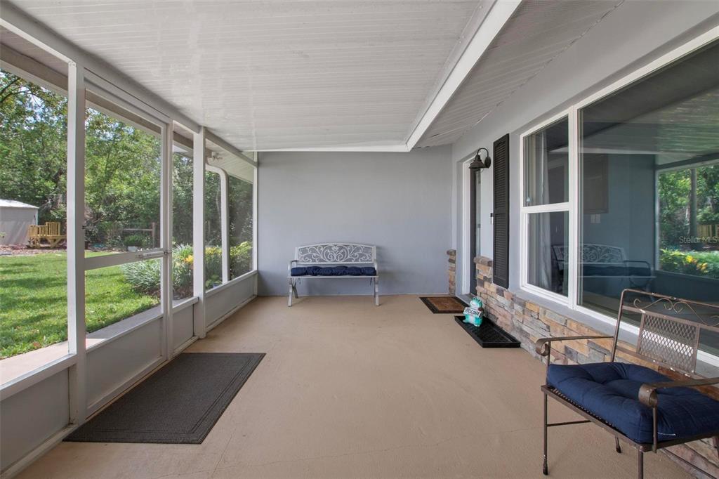 A screened-in porch with a concrete floor, a metal bench, and a view of a yard — 250 BRIGHAM ROAD NW, WINTER HAVEN, FL