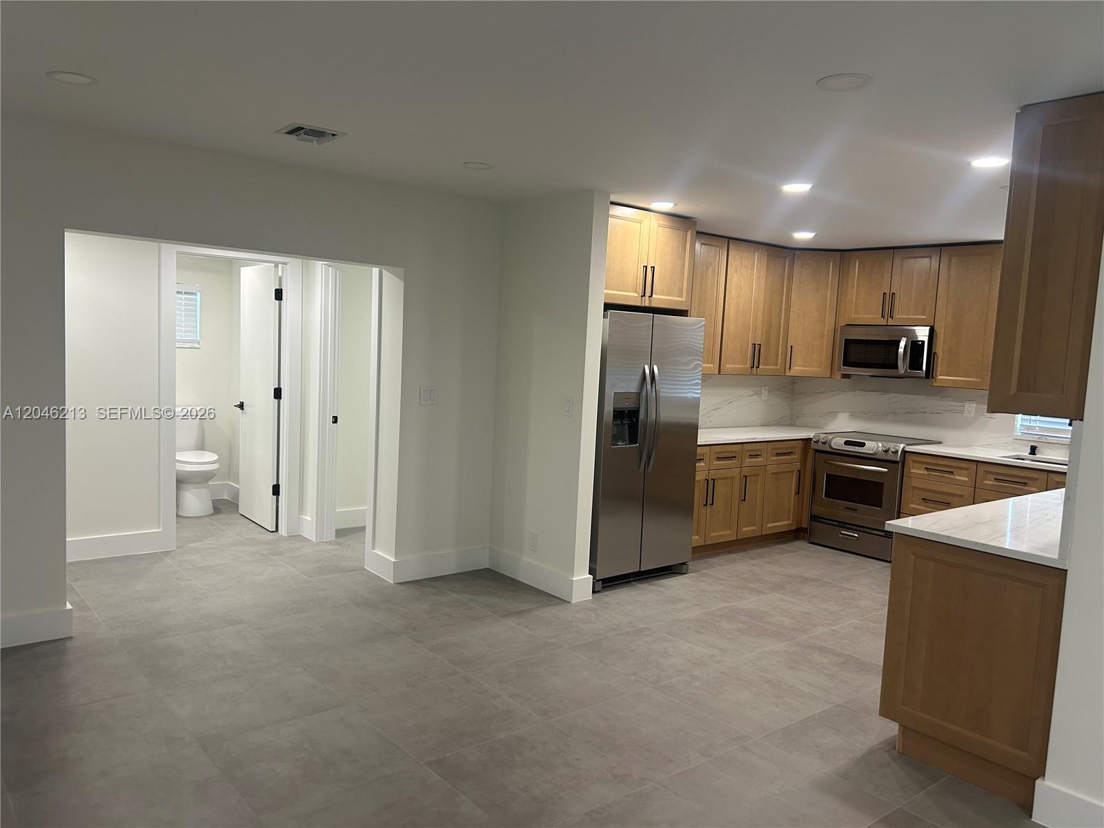 A kitchen with wood cabinets and stainless steel appliances opens to a hallway with bathrooms — 9723 SW 3rd St, Boca Raton FL 33428, BOCA RATON, FL