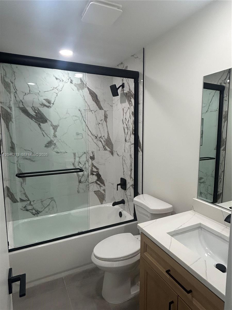 A modern bathroom features a marble-tiled shower, black fixtures, a white toilet, and wood vanity — 9723 SW 3rd St, Boca Raton FL 33428, BOCA RATON, FL