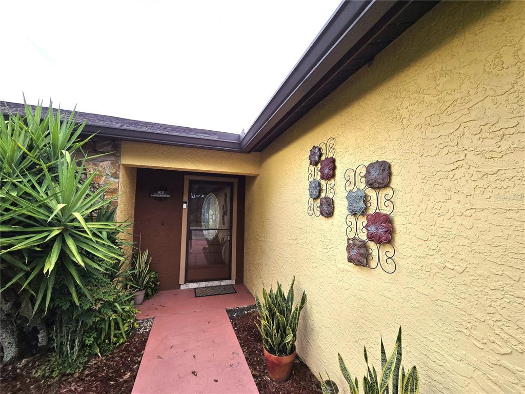 The exterior entryway features a yellow stucco wall, a red walkway, and decorative metal wall art — 812 SANDALWOOD DRIVE, PLANT CITY, FL