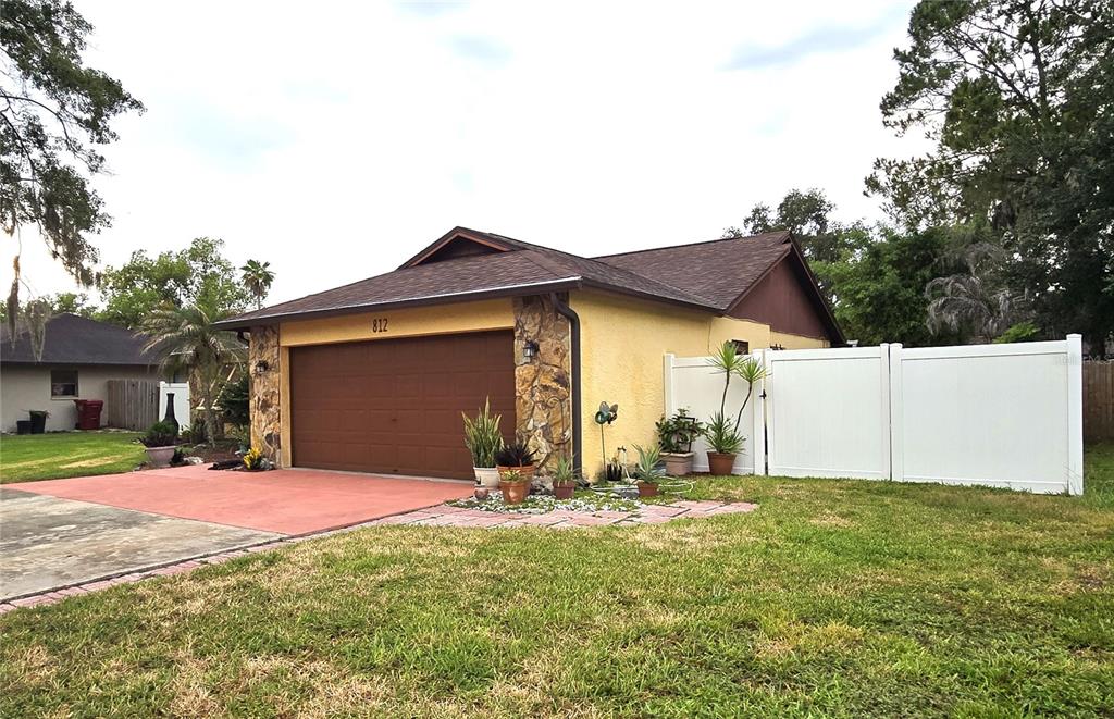 A single-story house with a yellow stucco exterior, stone accents, and a brown garage door — 812 SANDALWOOD DRIVE, PLANT CITY, FL