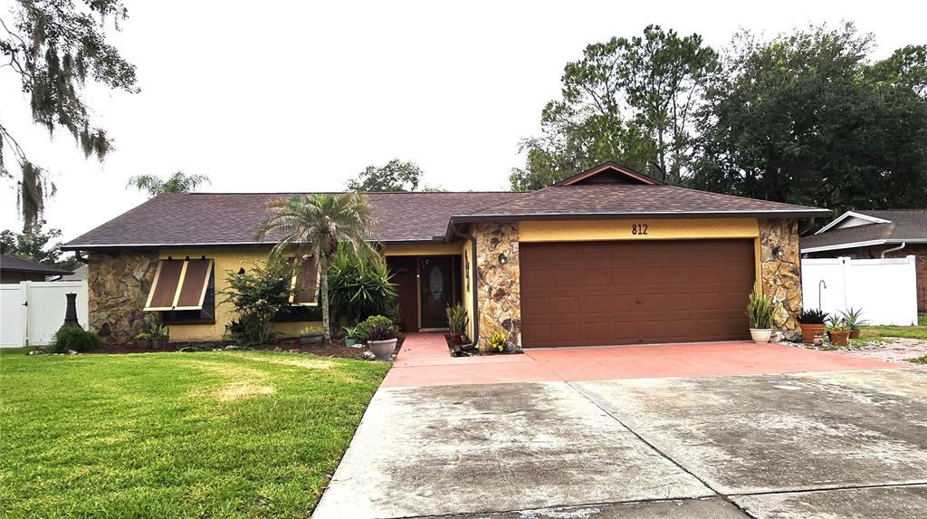 A single-story house with a stone facade, brown garage door, and a concrete driveway — 812 SANDALWOOD DRIVE, PLANT CITY, FL