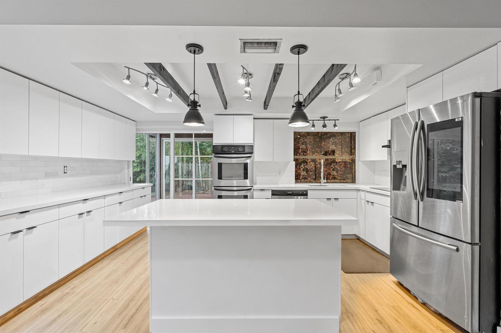 A modern white kitchen features a central island, stainless steel appliances, and dark ceiling beams — 5441 SW 155th Place, Miami FL 33185, MIAMI, FL