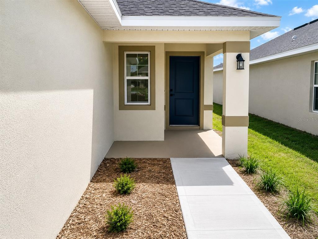 A front porch with a blue door, a concrete walkway, and a small landscaped garden — 7569 BENT TREE LOOP, ST CLOUD, FL