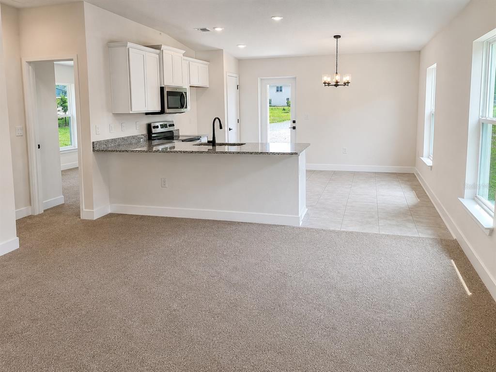 An open-concept kitchen with white cabinets and granite countertops overlooks a carpeted living area — 7569 BENT TREE LOOP, ST CLOUD, FL