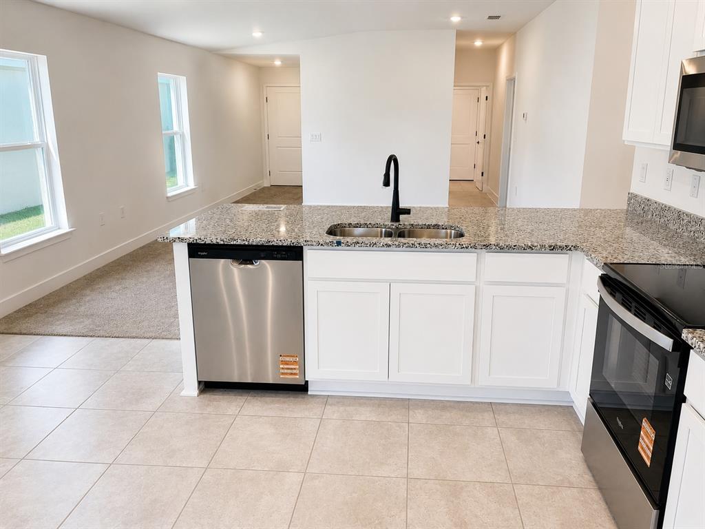 A kitchen with white cabinets, granite countertops, stainless steel appliances, and tile flooring — 7569 BENT TREE LOOP, ST CLOUD, FL