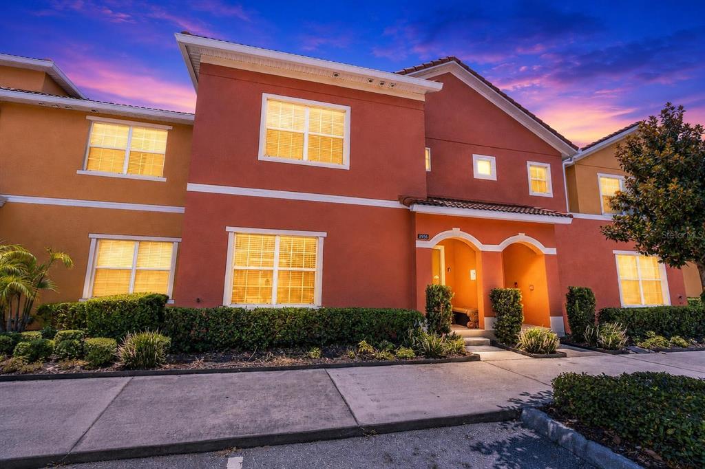 A two-story stucco townhouse exterior features orange walls, white trim, and a paved walkway — 8956 CALIFORNIA PALM ROAD, KISSIMMEE, FL