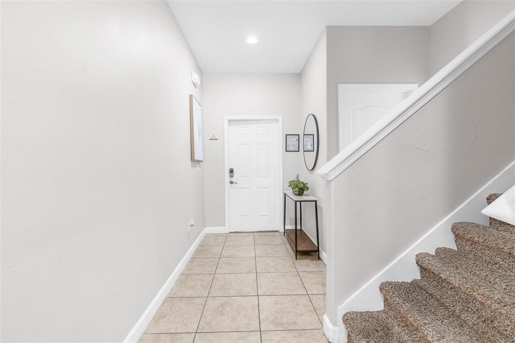 An entryway features tile flooring, a white front door, and a carpeted staircase — 8956 CALIFORNIA PALM ROAD, KISSIMMEE, FL