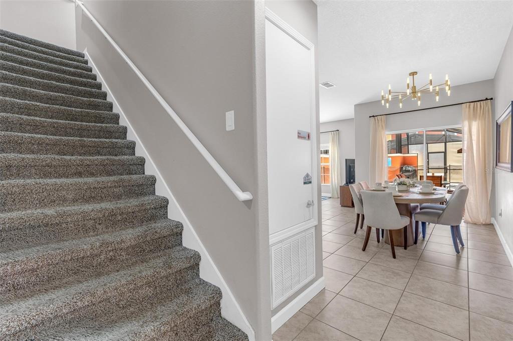 A carpeted staircase leads upward next to a dining area with tile flooring — 8956 CALIFORNIA PALM ROAD, KISSIMMEE, FL