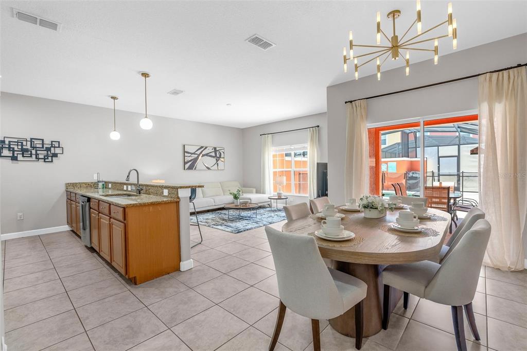 An open-concept kitchen, dining area, and living room featuring tile floors and a modern chandelier — 8956 CALIFORNIA PALM ROAD, KISSIMMEE, FL
