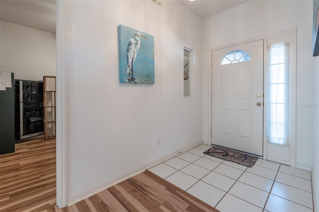 An entryway features white tile flooring, a white front door, and a heron wall painting — 9077 SW 95TH AVENUE, OCALA, FL