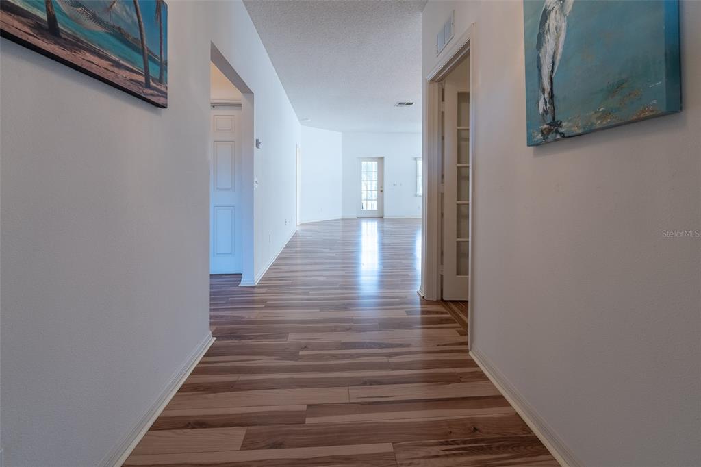 A hallway with wood-look flooring leads toward a bright room with a glass door — 9077 SW 95TH AVENUE, OCALA, FL