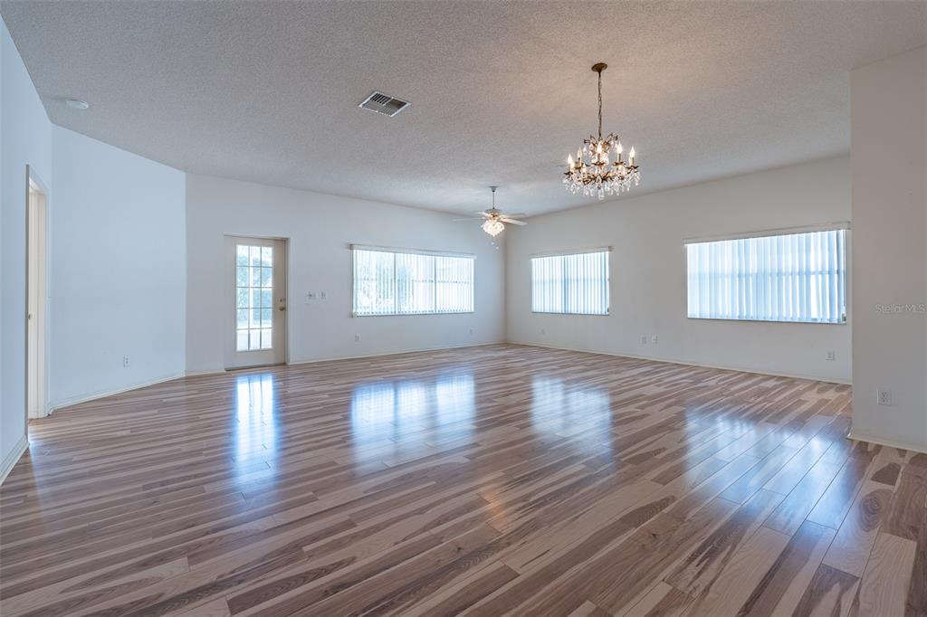 A spacious, empty living room features wood-look flooring, white walls, and two hanging light fixtures — 9077 SW 95TH AVENUE, OCALA, FL