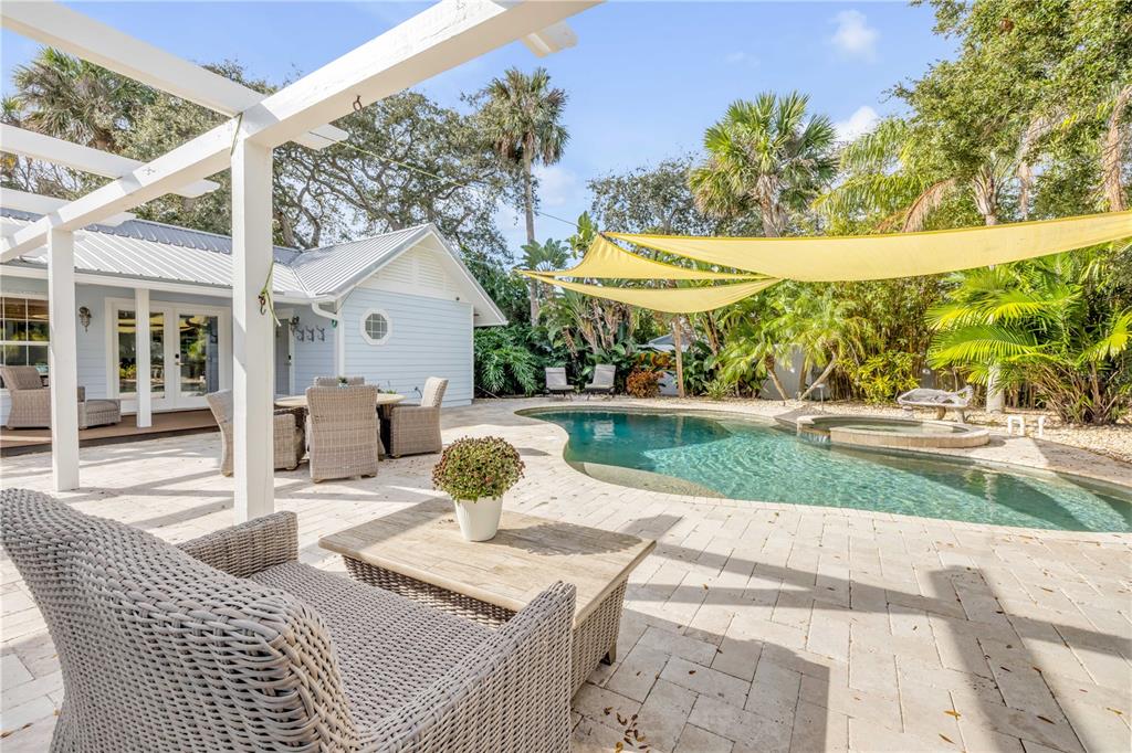 A backyard patio features a swimming pool, hot tub, yellow shade sails, and wicker furniture — 506 YUPON AVENUE, NEW SMYRNA BEACH, FL