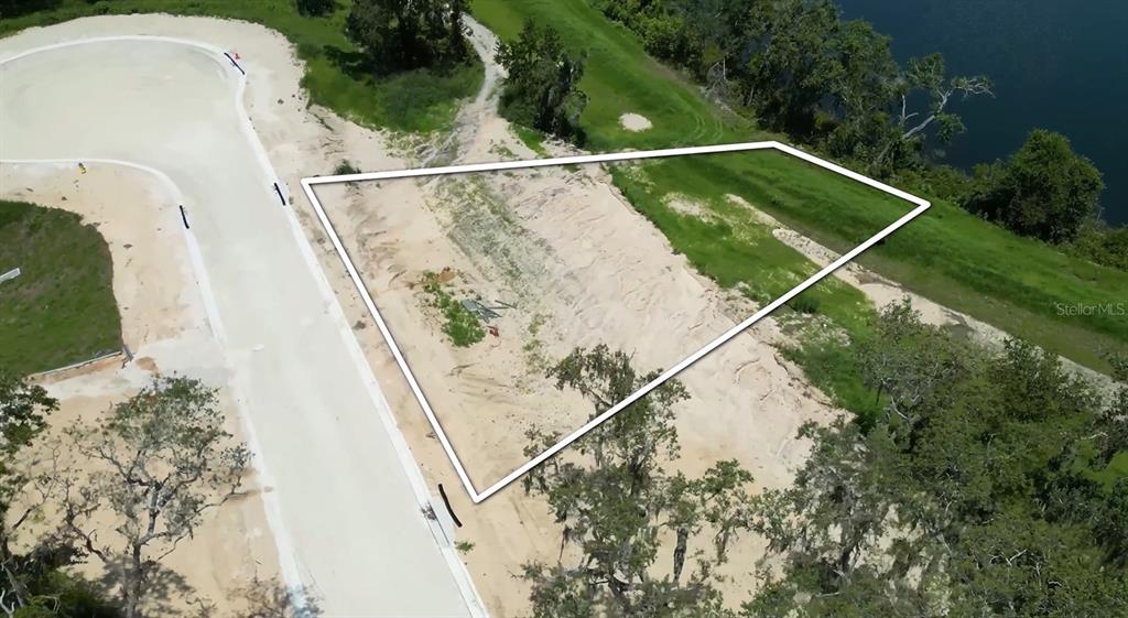 An aerial view shows a vacant, trapezoidal residential lot bordering a road and a lake — 145 TRANQUIL MIRROR LAKE COURT Lot 13, CLERMONT, FL