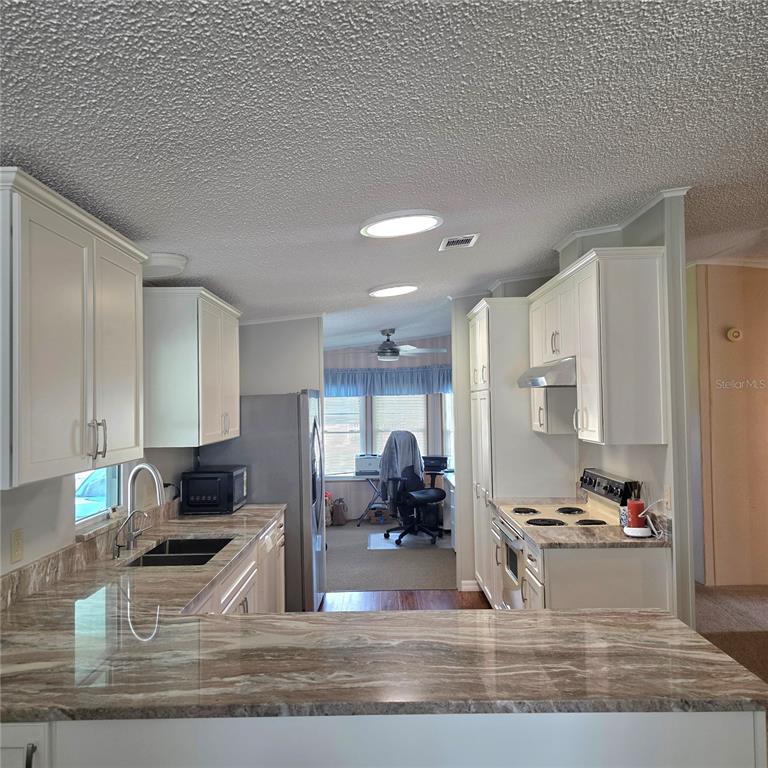 A kitchen with white cabinets and granite countertops overlooks a living area with a ceiling fan — 6114 GRAND OAKS DRIVE SE, WINTER HAVEN, FL