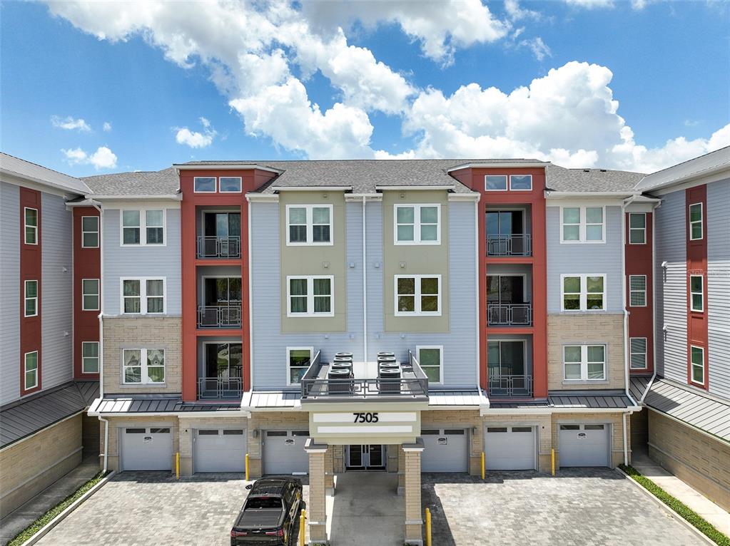 A multi-story apartment building features a paved driveway, several garage doors, and balconies — 7505 LAUREATE BLVD UNIT 2208, ORLANDO, FL