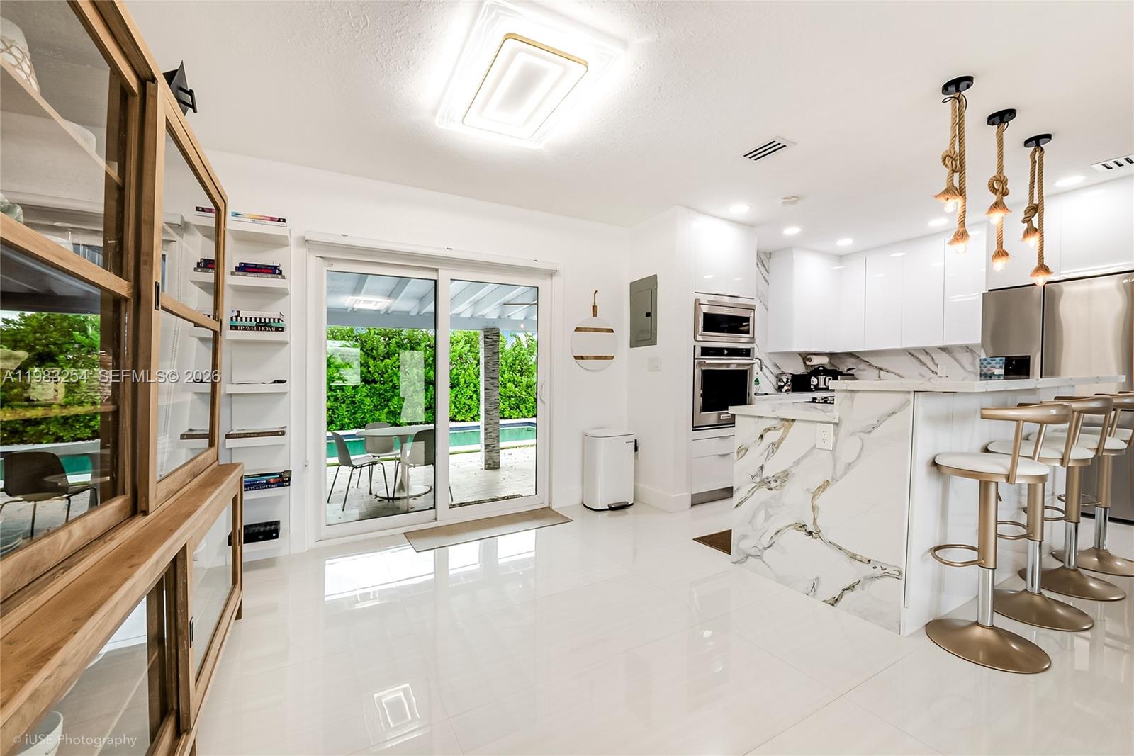 A modern kitchen features white cabinets, marble-patterned counters, and a sliding glass door to a patio — 7235 SW 39th St, Miami FL 33155, MIAMI, FL