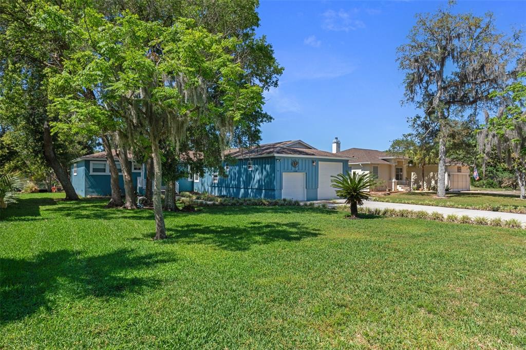 A blue house with a two-car garage sits on a large, grassy, tree-filled lot — 11430 W WATERWAY DRIVE, HOMOSASSA, FL