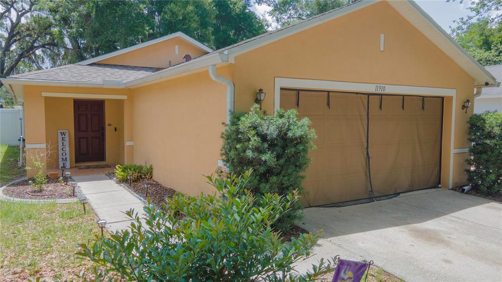 A single-story house with a tan stucco exterior, a brown front door, and a garage — 11910 MANGO GROVES BOULEVARD, SEFFNER, FL