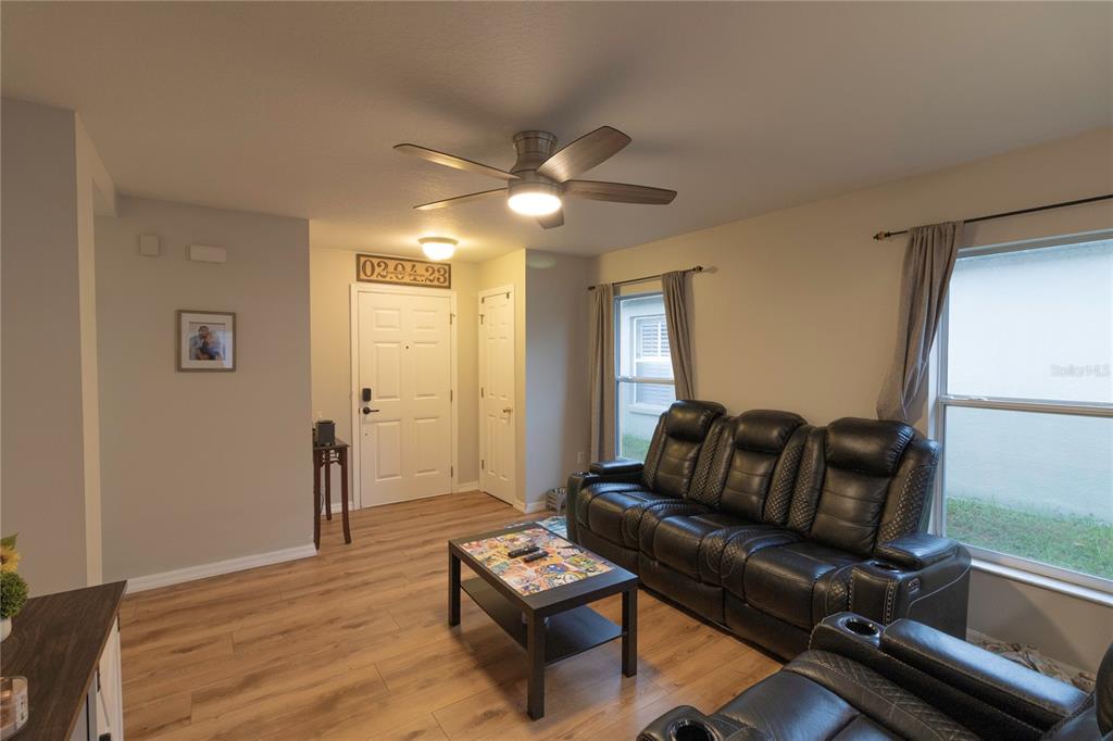 A living room features light wood-look flooring, a black leather sofa, and a ceiling fan — 11910 MANGO GROVES BOULEVARD, SEFFNER, FL