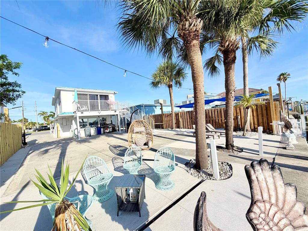 A paved outdoor patio area features palm trees, wicker chairs, and a small white building — 17729 GULF BOULEVARD, REDINGTON SHORES, FL