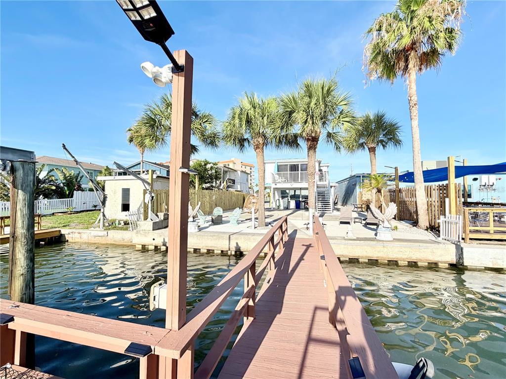A wooden dock leads to a waterfront patio area with palm trees and outdoor furniture — 17729 GULF BOULEVARD, REDINGTON SHORES, FL