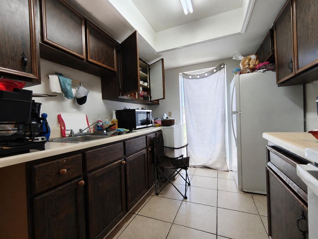A kitchen features dark wood cabinets, white countertops, tile flooring, and a white refrigerator — 39 LAGO MESA WAY, KISSIMMEE, FL