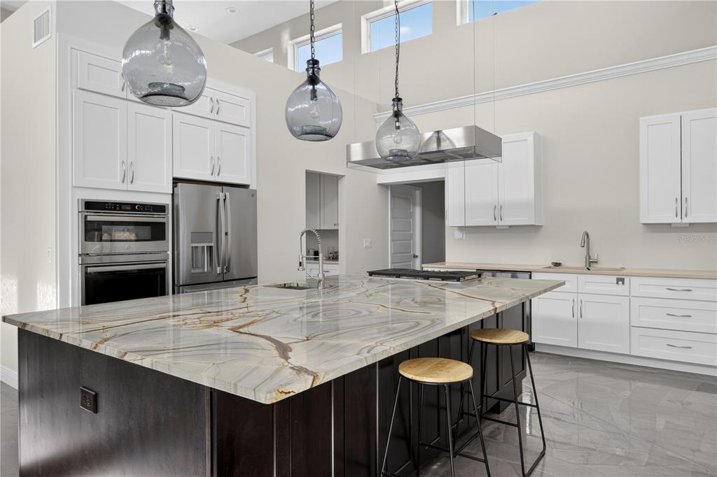 A kitchen features a large stone island, dark cabinetry, white upper cabinets, and glass pendant lights — 13002 CROWELL ROAD, BROOKSVILLE, FL