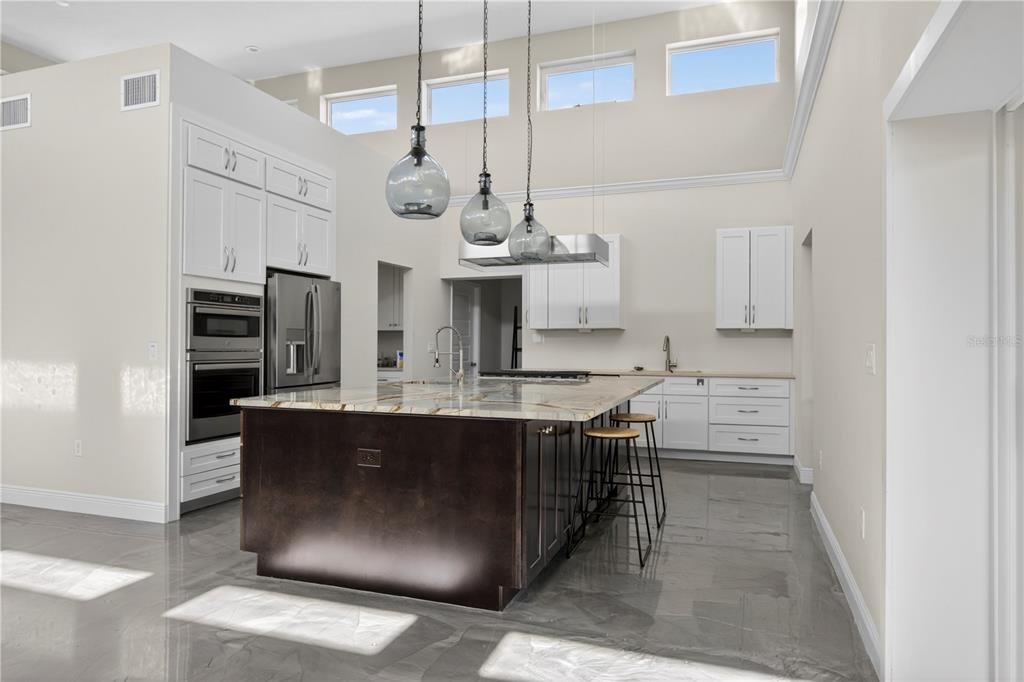A modern kitchen features a dark wood island, white cabinetry, stainless appliances, and high ceilings — 13002 CROWELL ROAD, BROOKSVILLE, FL