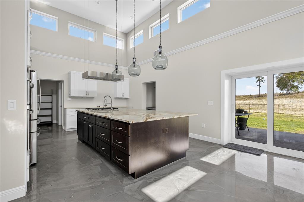 A modern kitchen features a dark wood island, white cabinets, and high ceilings with windows — 13002 CROWELL ROAD, BROOKSVILLE, FL