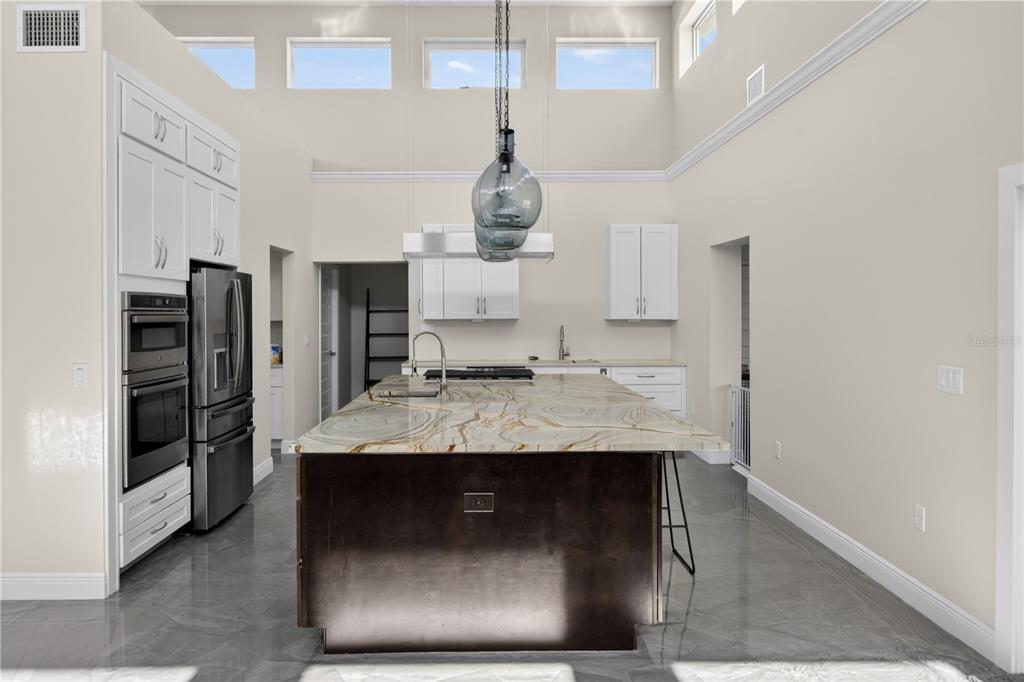 A modern kitchen features a large stone-topped island, dark cabinetry, and high ceilings with clerestory windows — 13002 CROWELL ROAD, BROOKSVILLE, FL