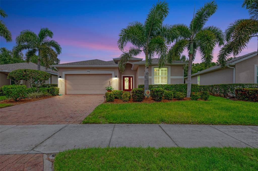A single-story house with a brick driveway, palm trees, and a two-car garage at dusk — 9082 COACHMAN DRIVE, VENICE, FL