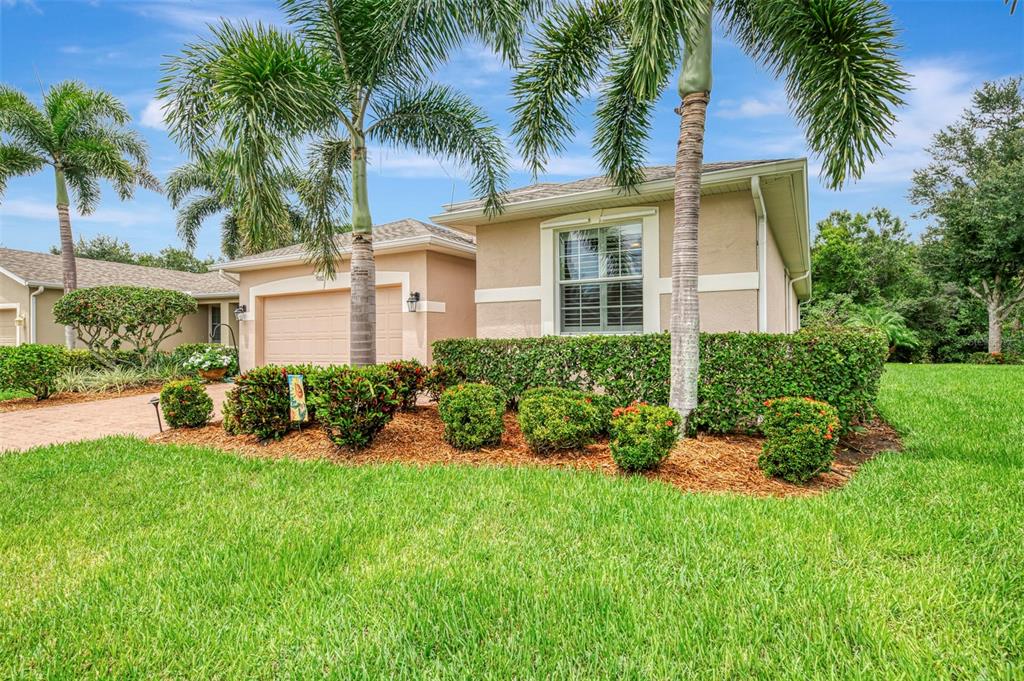 A single-story house with a tan exterior, a two-car garage, and palm trees in front — 9082 COACHMAN DRIVE, VENICE, FL