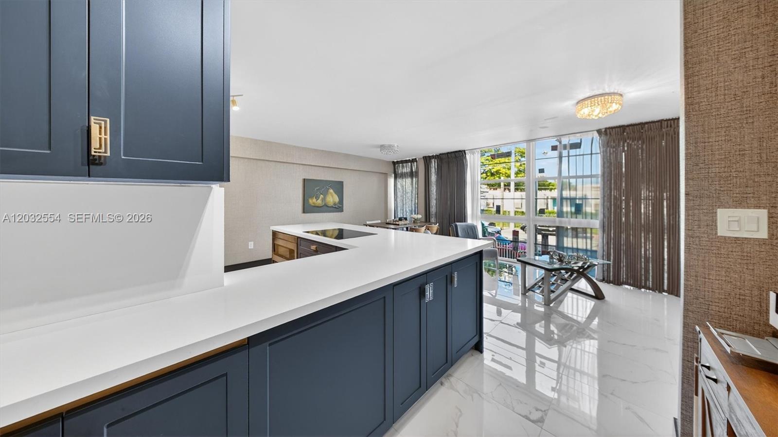 A kitchen with dark blue cabinets and white countertops overlooks a bright living area — 1400 Pennsylvania Ave # 11, Miami Beach FL 33139, MIAMI BEACH, FL