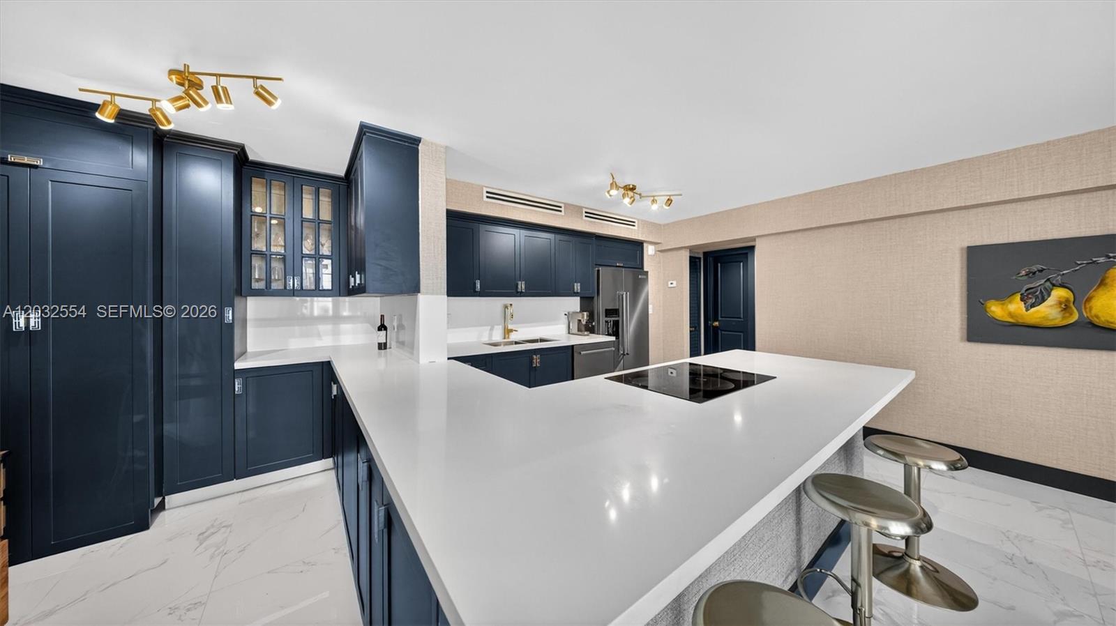 A modern kitchen features dark blue cabinetry, white countertops, and a central island with stools — 1400 Pennsylvania Ave # 11, Miami Beach FL 33139, MIAMI BEACH, FL
