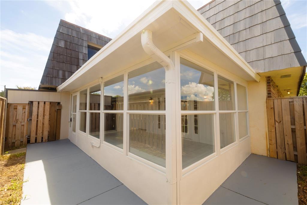A white-framed sunroom with large windows sits on a gray concrete patio beside wooden fencing — 2947 POPLAR AVENUE, LEESBURG, FL